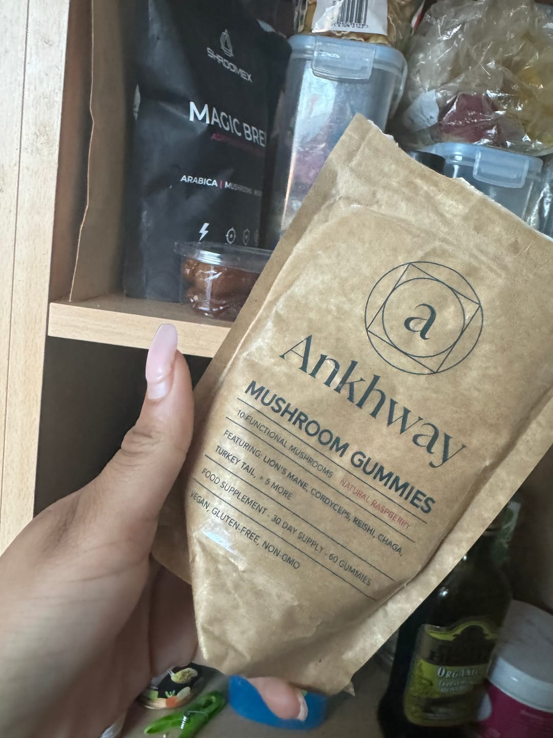 A hand holding a bag of Ankhway Mushroom Gummies in front of a pantry.