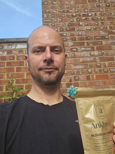 Man holding a packet of Ankhwand Mushroom Gummies in front of a brick wall.